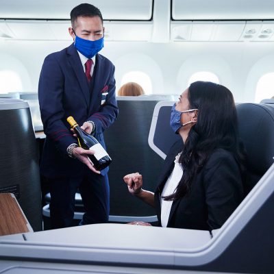 A flight attendant offers a business-woman a glass of complimentary champagne